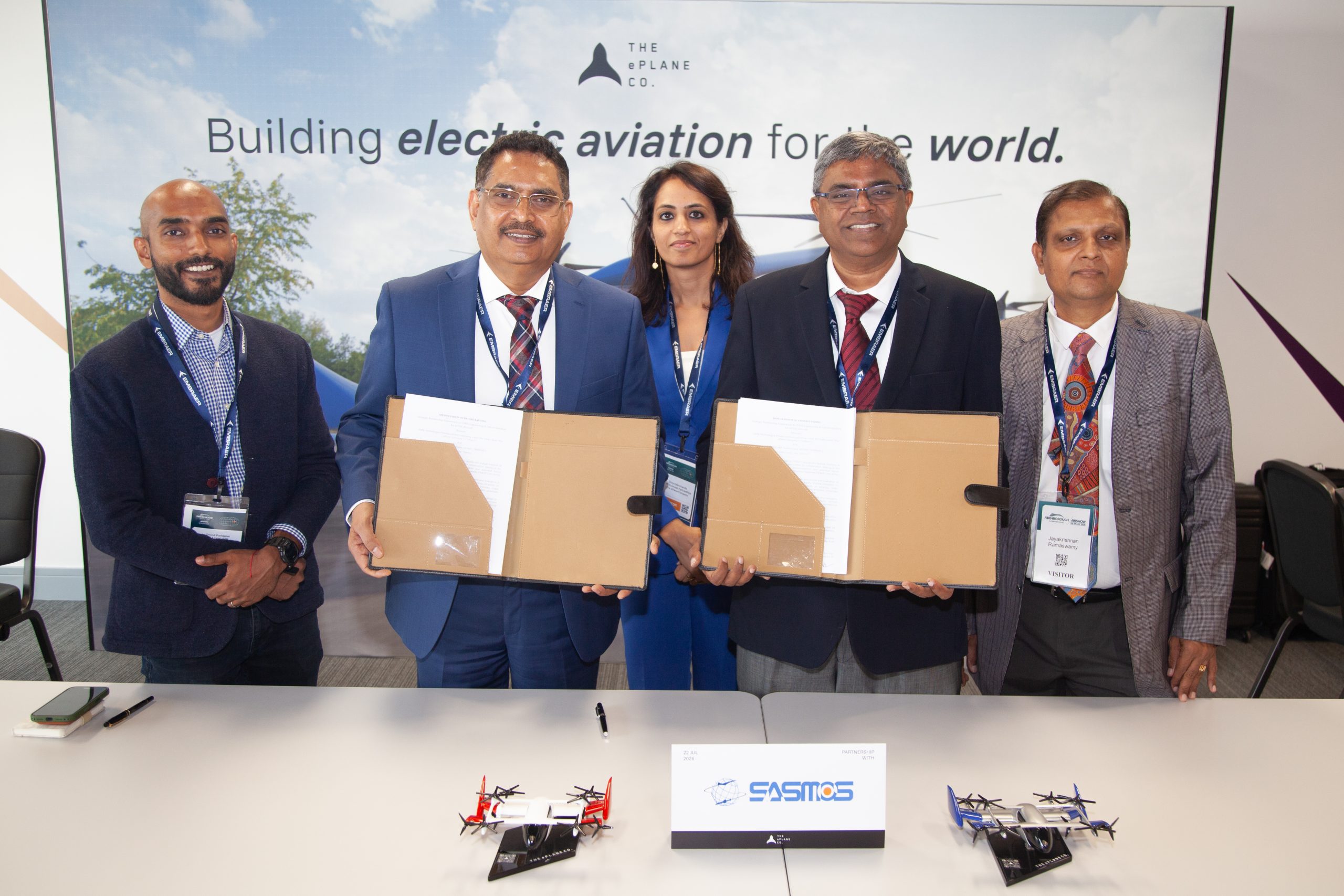 Five professionals in business attire stand behind a table holding large folders, posing for a group photo at an aviation event.