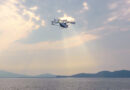 Light helicopter flying above a calm body of water with low hills on the horizon at sunset