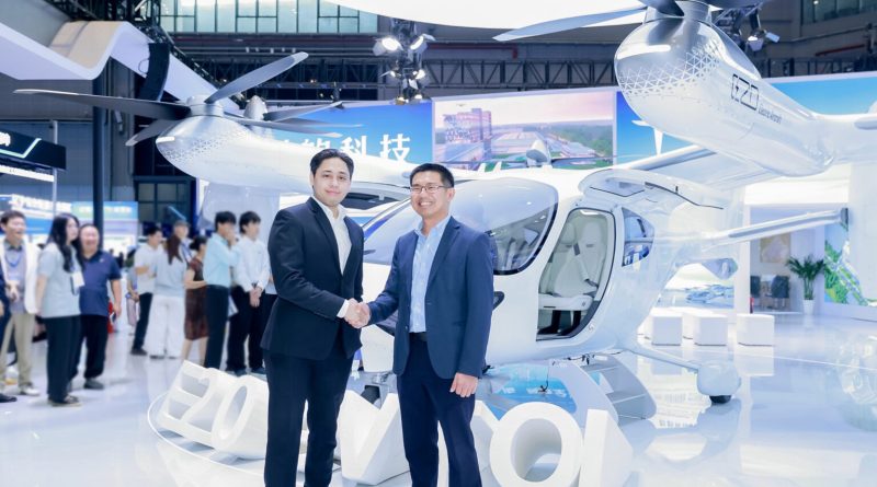 Two businessmen in suits shake hands in front of a white helicopter at an indoor expo, with attendees in the background.