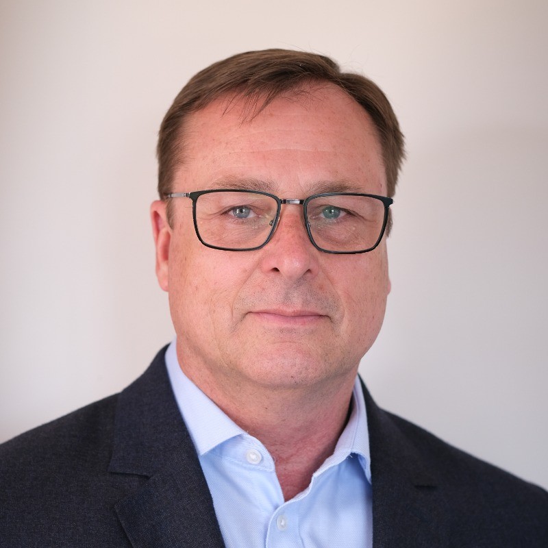 Anthony Venetz profile - eVTOL Insights Head-and-shoulders portrait of a middle-aged man in glasses with a blue shirt and dark blazer, smiling softly.