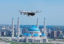 AutoFlight Astana1 - eVTOL Insights Autonomous aerial drone flying over a city with blue-domed mosques and tall minarets at sunset.",