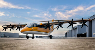 Orange and white multi-propeller aircraft parked on a tarmac beside hangars, under a blue sky.