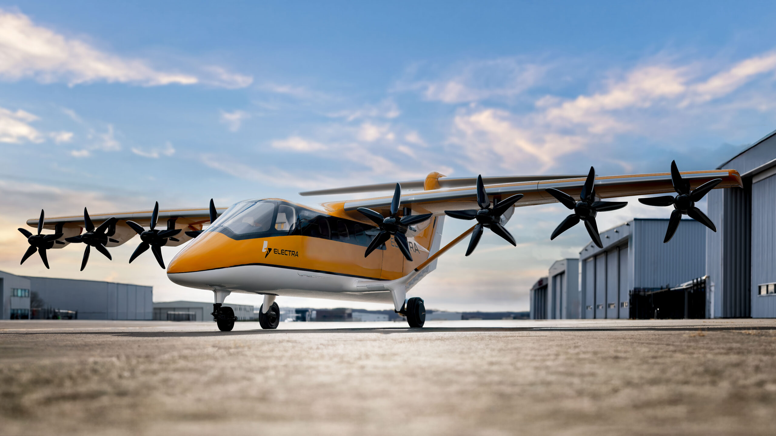 Orange and white multi-propeller aircraft parked on a tarmac beside hangars, under a blue sky.
