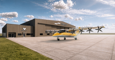 Yellow twin‑engine Electra aircraft parked on a concrete apron beside a brown Signature Aviation hangar under a blue sky.