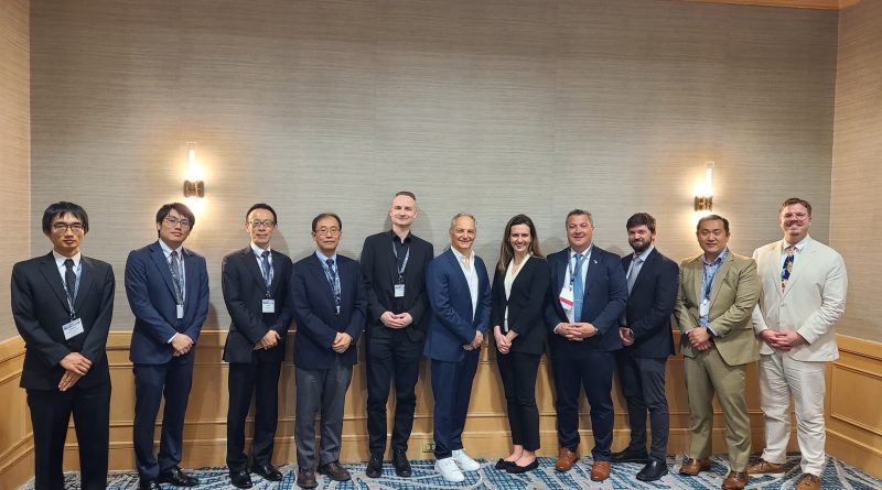 Group of professionally dressed individuals standing in a line for a formal photo in a conference room, all wearing name badges.