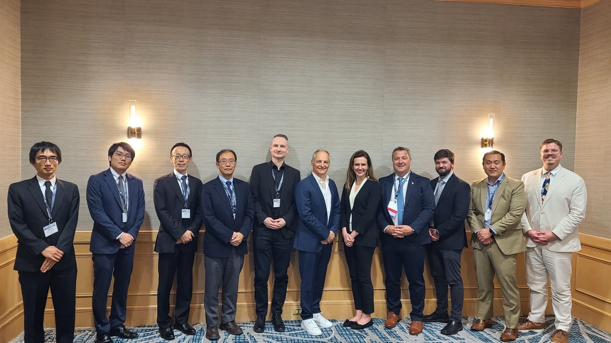 Group of professionally dressed individuals standing in a line for a formal photo in a conference room, all wearing name badges.