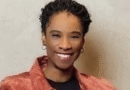 Smiling woman with short curly hair wearing a red jacket over a black top, facing the camera.