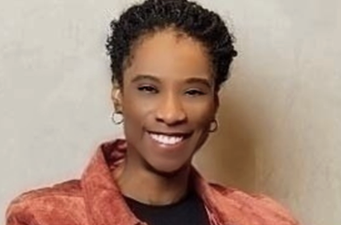 Smiling woman with short curly hair wearing a red jacket over a black top, facing the camera.