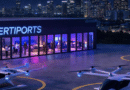 Nighttime VertiPorts facility with a glass-front lounge, people inside, and helicopters on the tarmac under city lights.