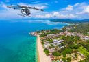 Small white quadrotor helicopter flying over a tropical coastline with a sandy beach below