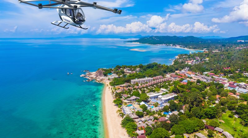 Small white quadrotor helicopter flying over a tropical coastline with a sandy beach below
