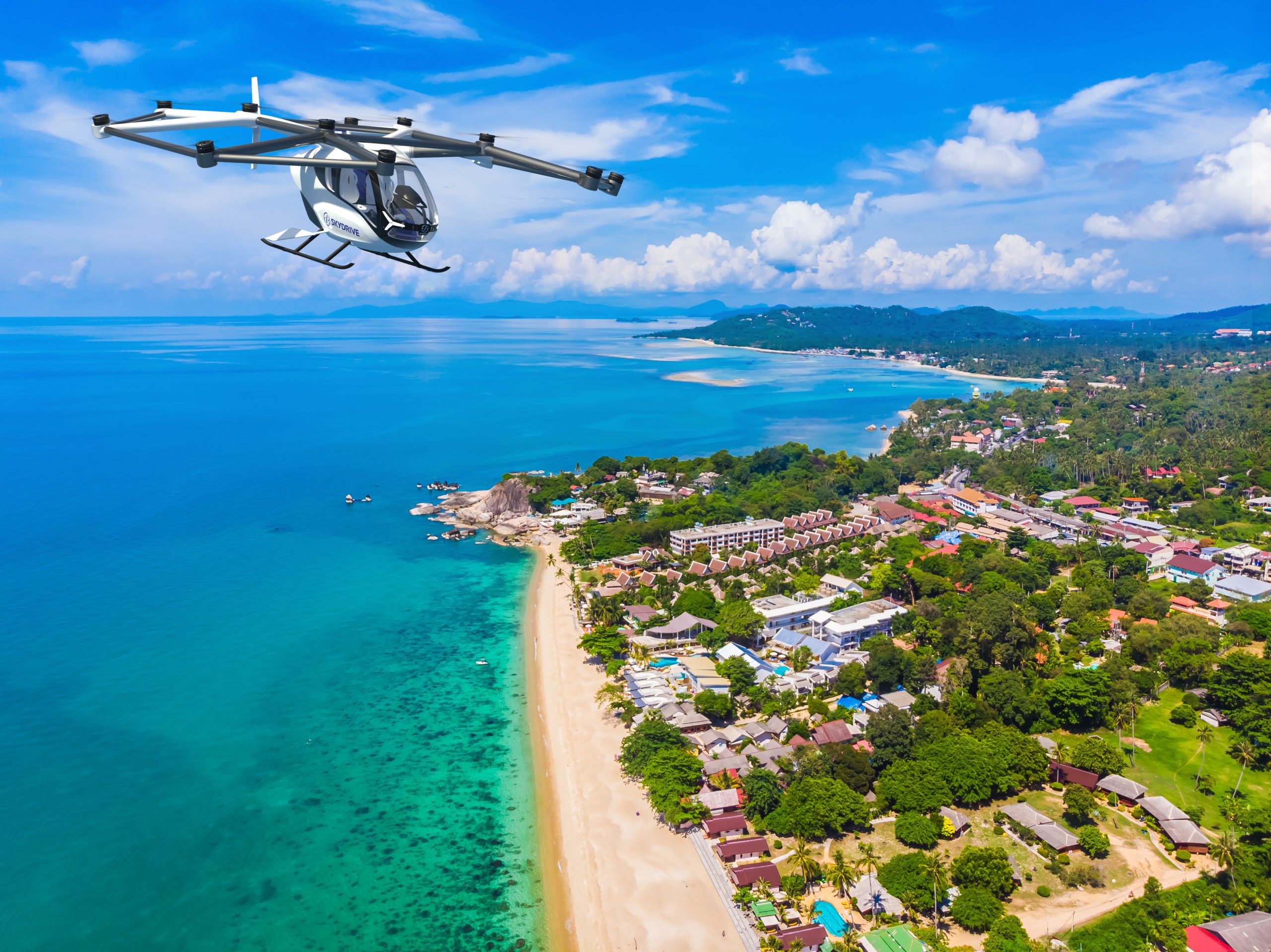 Small white quadrotor helicopter flying over a tropical coastline with a sandy beach below