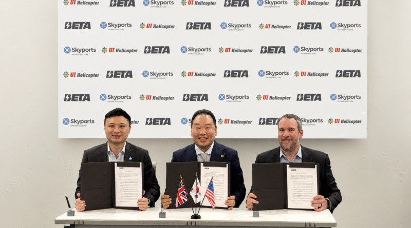 Three men in suits sit at a table holding signed documents during a formal agreement ceremony, flags in front, backdrop with logos behind them.