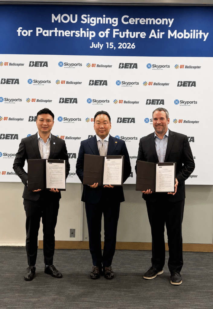 Three men in business suits stand in front of a blue banner that reads'MOU Signing Ceremony for Partnership of Future Air Mobility July 15, 2026,' each holding an open binder with a signed document. The backdrop features repeated logos (Skyports, BETA, UI Helicopter).