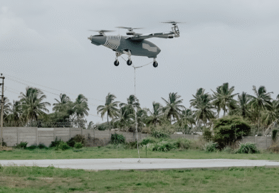Sylla Flight Test Campaign - eVTOL Insights Large four-rotor drone hover-lift with a tether descending to the ground over a concrete pad, palm trees in the background.