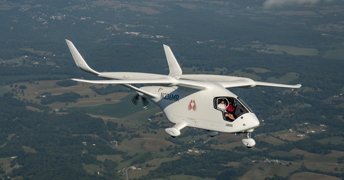 White small aircraft in flight over a patchwork countryside, two people visible in the cockpit smiling at the camera, registration N336MR.