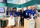 avtrain-farnborough - eVTOL Insights Group of staff at a trade show booth posing for a photo; several wearing blue Avtrain polo shirts with lanyards and badges.