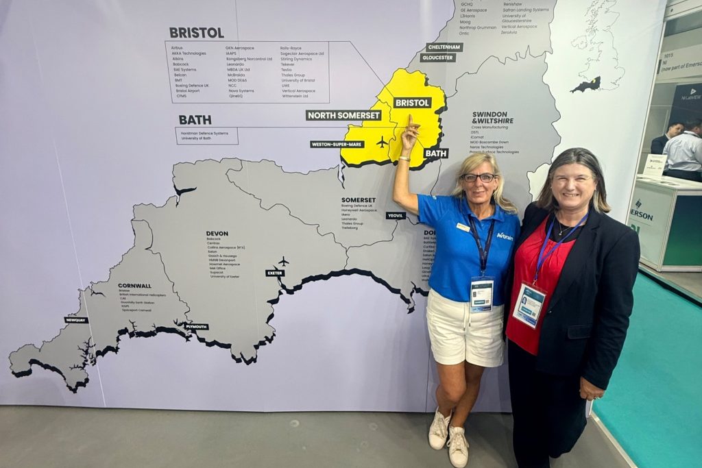 avtrain-farnborough-2 - eVTOL Insights Two women with lanyards pose beside a large map wall highlighting Bristol and Bath; one points at the map.