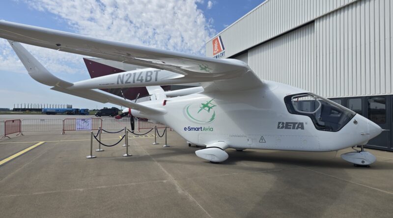 White small aircraft with N214BT registration parked on tarmac beside a corrugated metal hangar, e-Smart Avia branding visible on fuselage