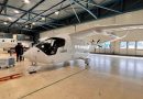 ClearSky Airlines Plans Europe’s First All-Electric Cargo Network for 2027 Interior of a large aircraft hangar with a white, futuristic plane in the foreground and two men in suits inspecting it, a second plane visible in the background