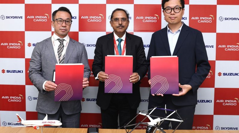 Air India, SkyDrive and Suzuki Sign MoU forFeasibility Study of Medical Air Logistics in India Three men in suits hold red folders at a formal event, standing before a red-and-white branded backdrop (Air India Cargo, Suzuki).