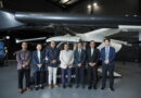 Group of professionals posing in front of a large helicopter inside a showroom or exhibit hall.