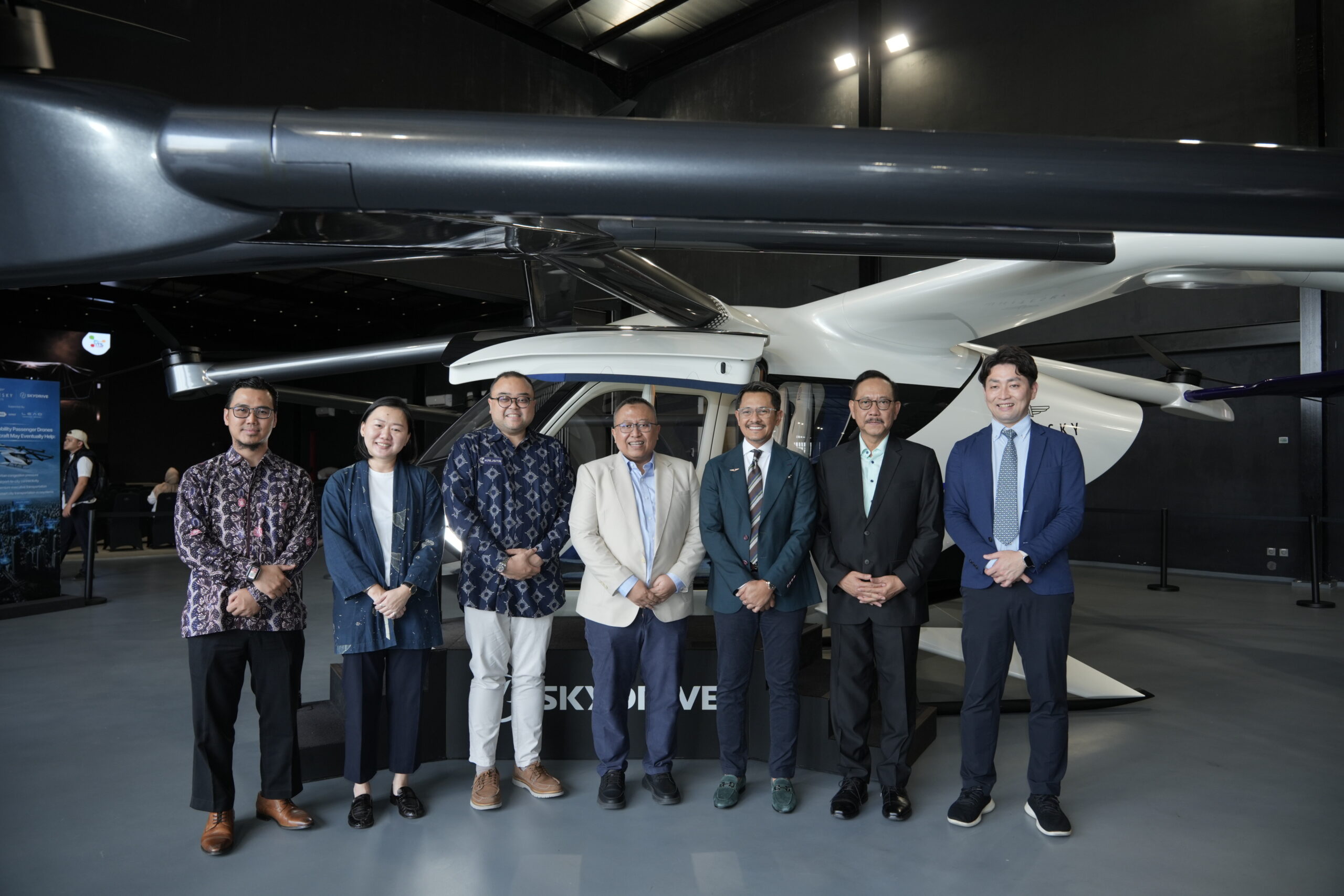 Group of professionals posing in front of a large helicopter inside a showroom or exhibit hall.