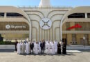 Group of men and women in traditional white kanduras and black abayas pose for a photo in front of a modern building with Skyports signage and a central circular logo.
