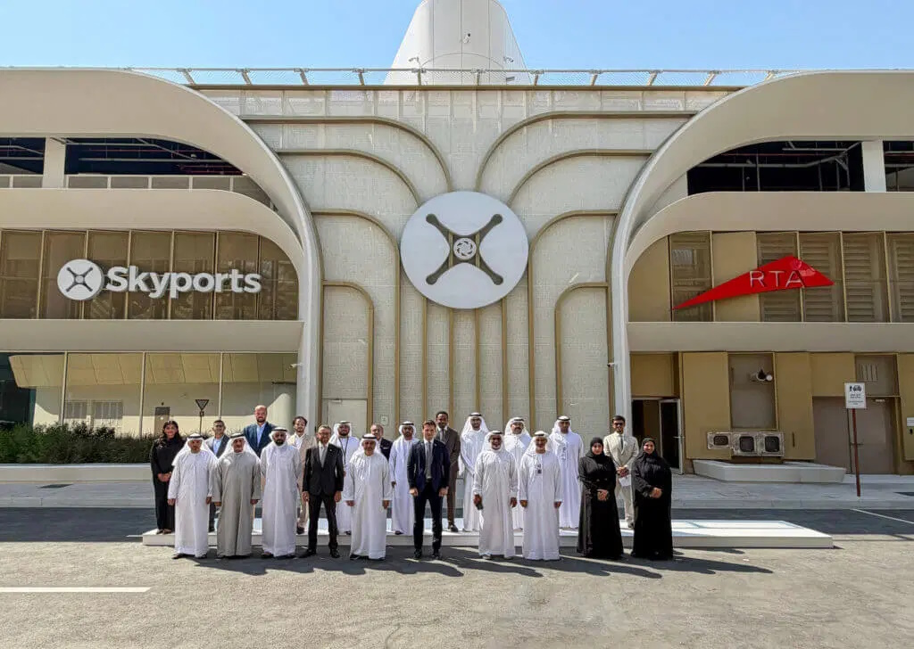 Group of men and women in traditional white kanduras and black abayas pose for a photo in front of a modern building with Skyports signage and a central circular logo.