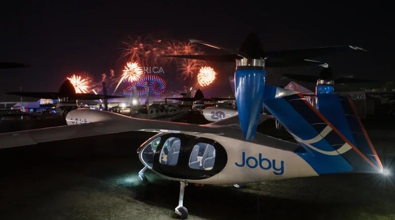 Night scene at an air show with a Joby eVTOL aircraft in the foreground and colorful fireworks in the background.