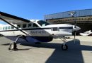 Small white and blue experimental propeller airplane on the tarmac in front of a blue AMPAIRE hangar.”