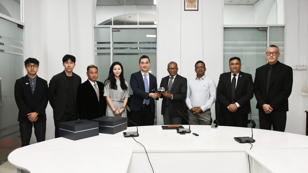 EHANG fast track delegation - eVTOL Insights Group of professionals in formal attire standing behind a conference table in an office, posing for a photo with two boxed items visible on the table behind them