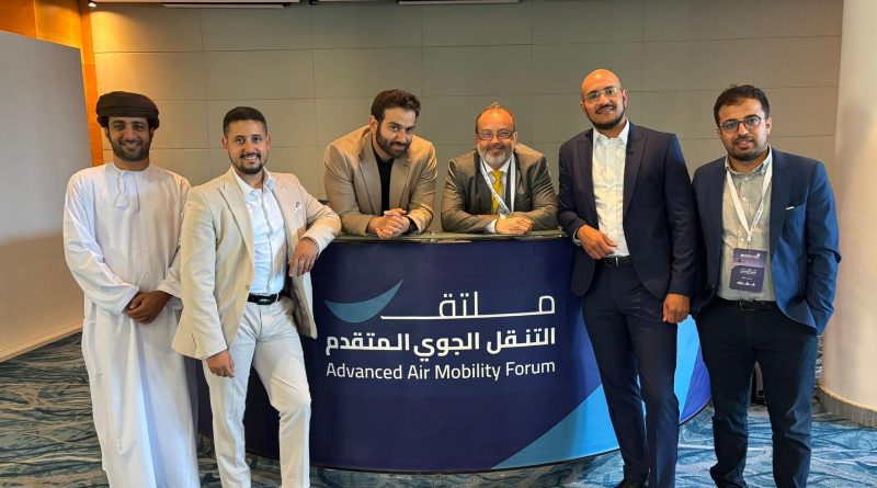 Six men pose behind a purple banner that reads 'Advanced Air Mobility Forum' in English and Arabic, at a conference retreat setting.