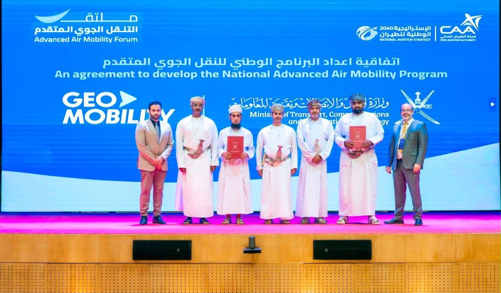Group of men in traditional dishdashas and suits stand on a stage receiving awards, with a blue backdrop showing the Advanced Air Mobility Forum logo.