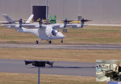 White tilt-rotor aircraft with four rotors taxiing on a runway; an inset photo in the lower-right shows two people seated inside a cabin. The aircraft bears registration G-EVIA and is near a hangar on a sunny day.