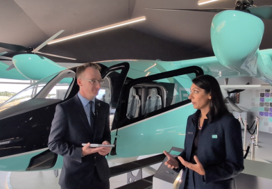 Two professionals in business attire stand beside a teal helicopter inside a showroom, talking.
