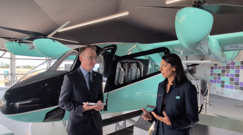 Two professionals in business attire stand beside a teal helicopter inside a showroom, talking.