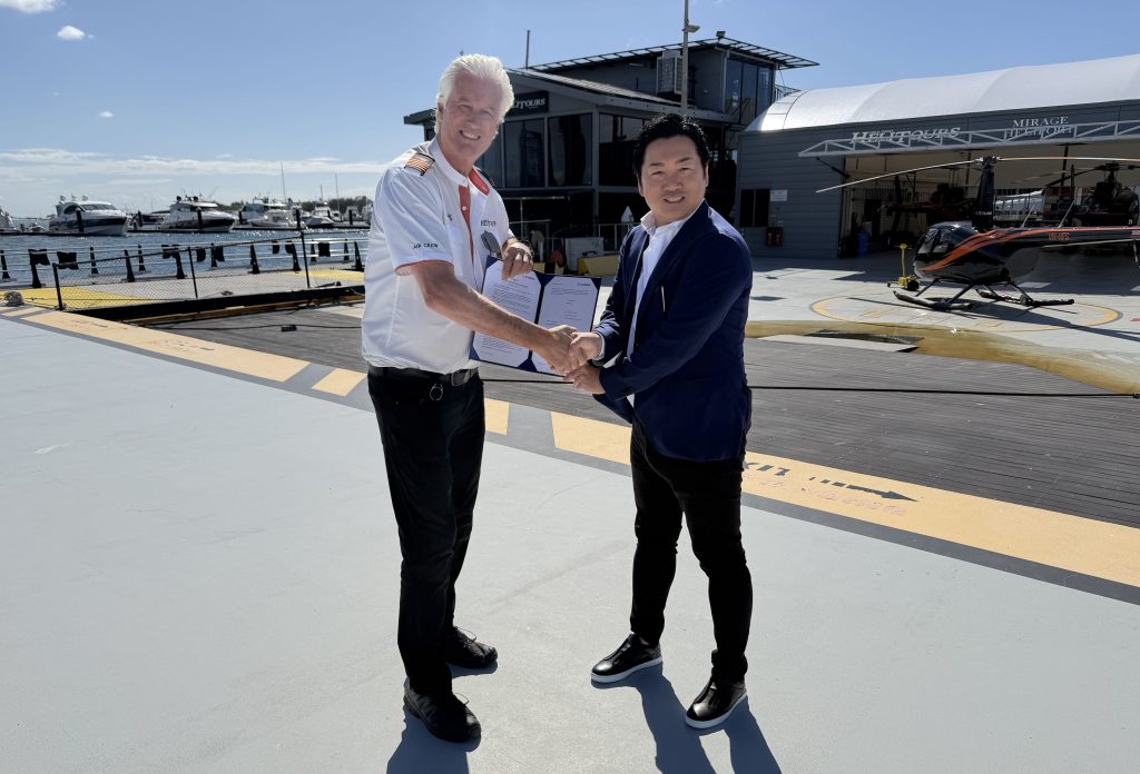 Two men shake hands on a helipad with boats and a marina in the background.