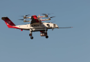 Elroy Air cargo drone with six rotor arms in midflight over a blue sky, carrying a payload beneath the fuselage.