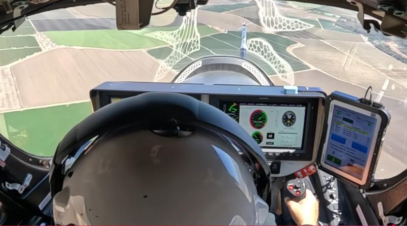 View inside a crop-dusting aircraft cockpit: pilot wearing a helmet, two screens with gauges, and a joystick with farmland visible ahead.
