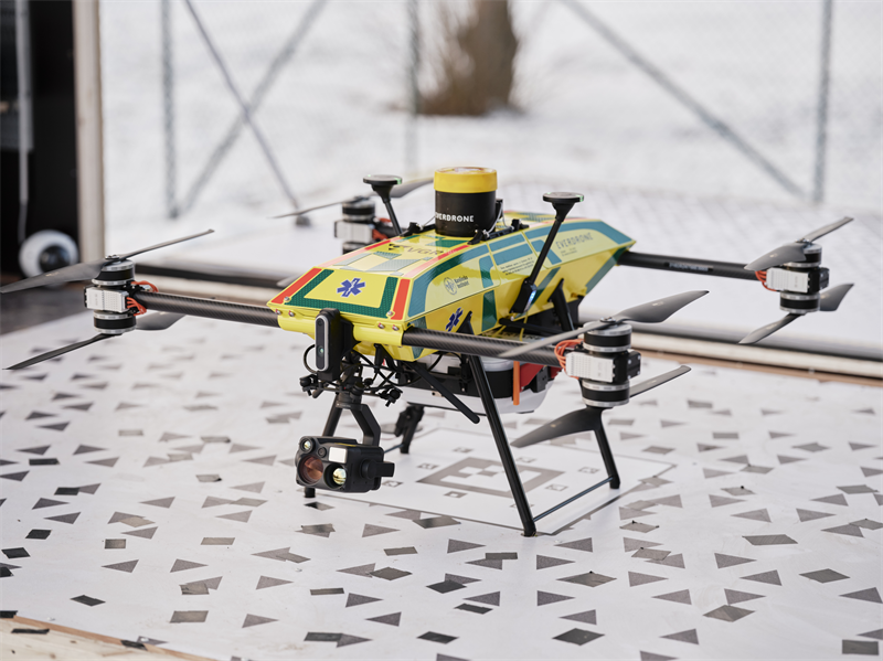 Yellow quadcopter drone with medical markings and mounted camera sits on a patterned table outdoors.
