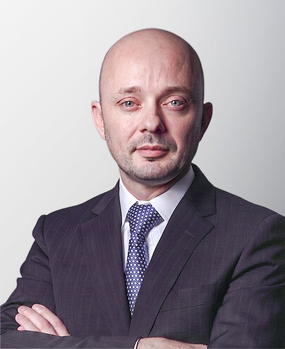 image 2 - eVTOL Insights Professional head-and-shoulders portrait of a bald man in a dark pinstriped suit with a blue patterned tie, arms crossed in front of a neutral background