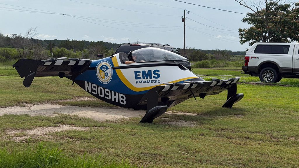 EMS paramedic aircraft on a grassy airstrip with a pilot visible in the cockpit; tail number N909HB, a white pickup truck nearby in a rural setting.