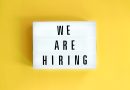 Lightbox sign on a yellow background reading 'WE ARE HIRING' in bold letters.