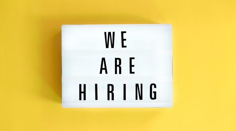 Lightbox sign on a yellow background reading 'WE ARE HIRING' in bold letters.