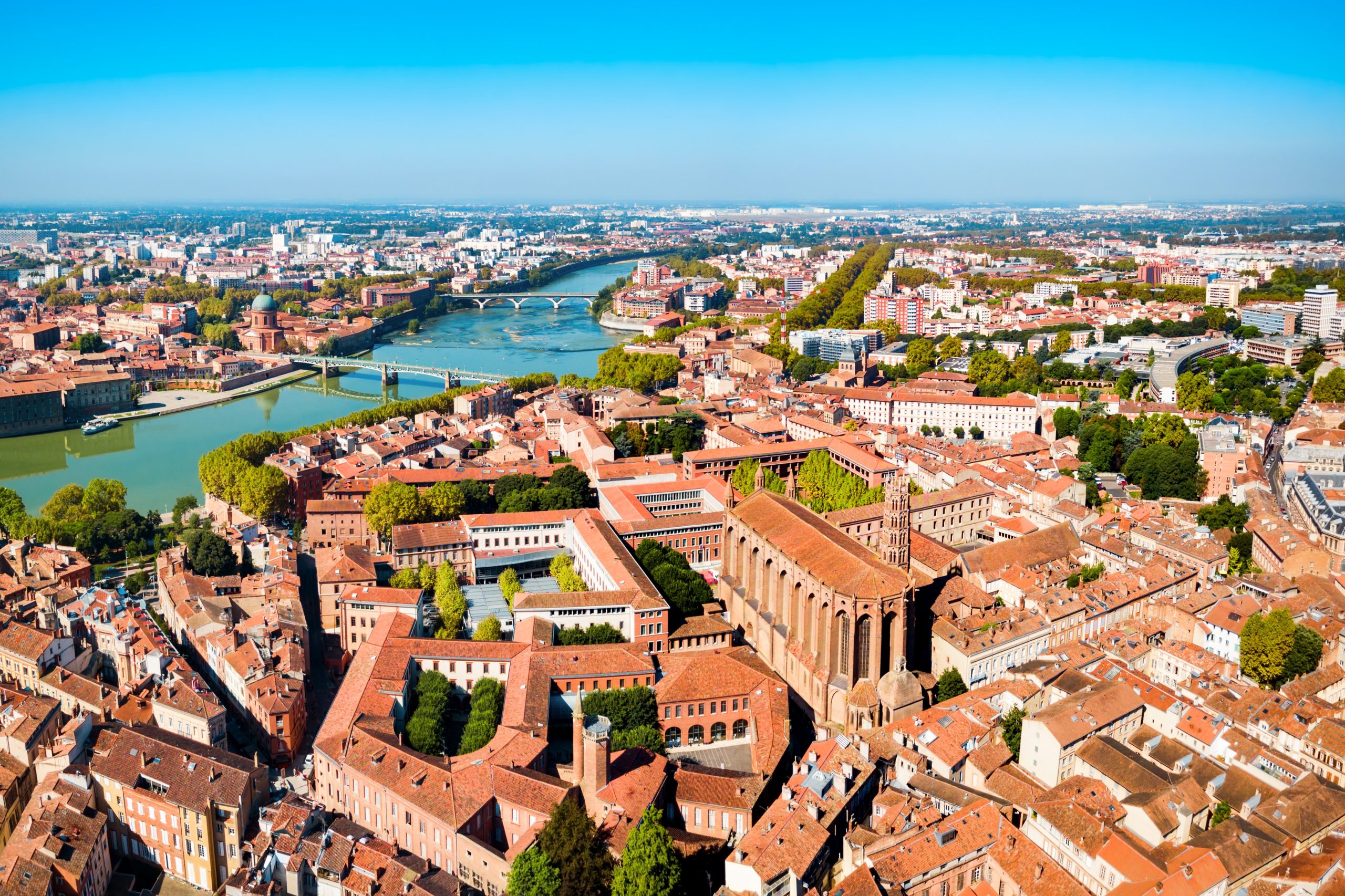 Aerial view of a city with a winding river, several bridges, and dense red-roofed buildings.