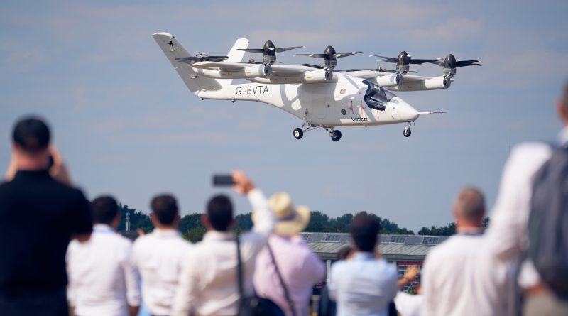 Tiltrotor Osprey aircraft flying low over spectators at an air show, crowd capturing the moment with phones and cameras.